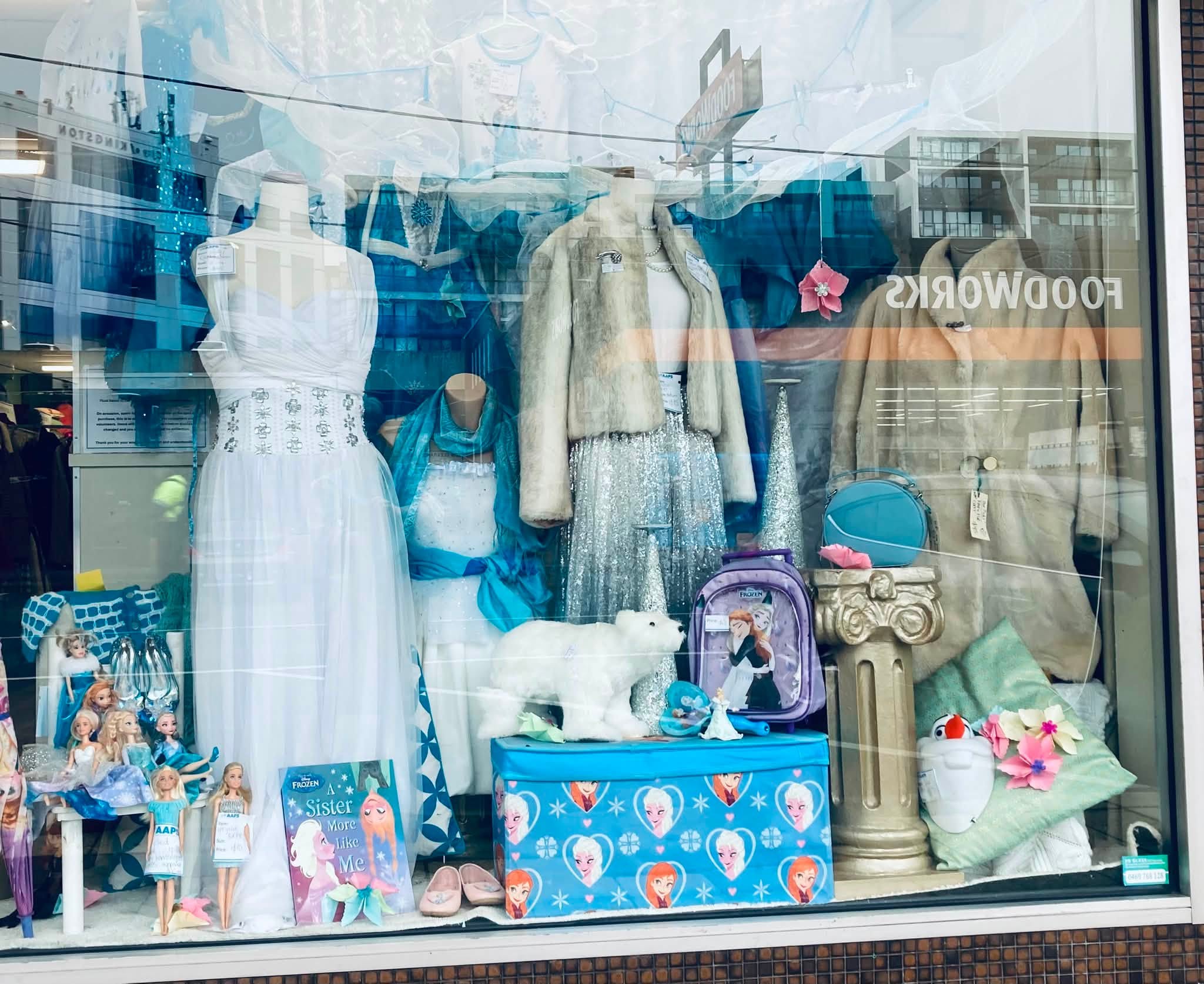 Frozen frenzy at AAPS Op Shop Cheltenham, with children’s Elsa and Anna costumes, dolls, toys, glitter shoes and wintery clothing in store. Visible prices include a Frozen backpack for $5, a polar-bear soft toy for $8, an upcycled doll for $10, and a white crystal dress in size 12–14 for $45.
