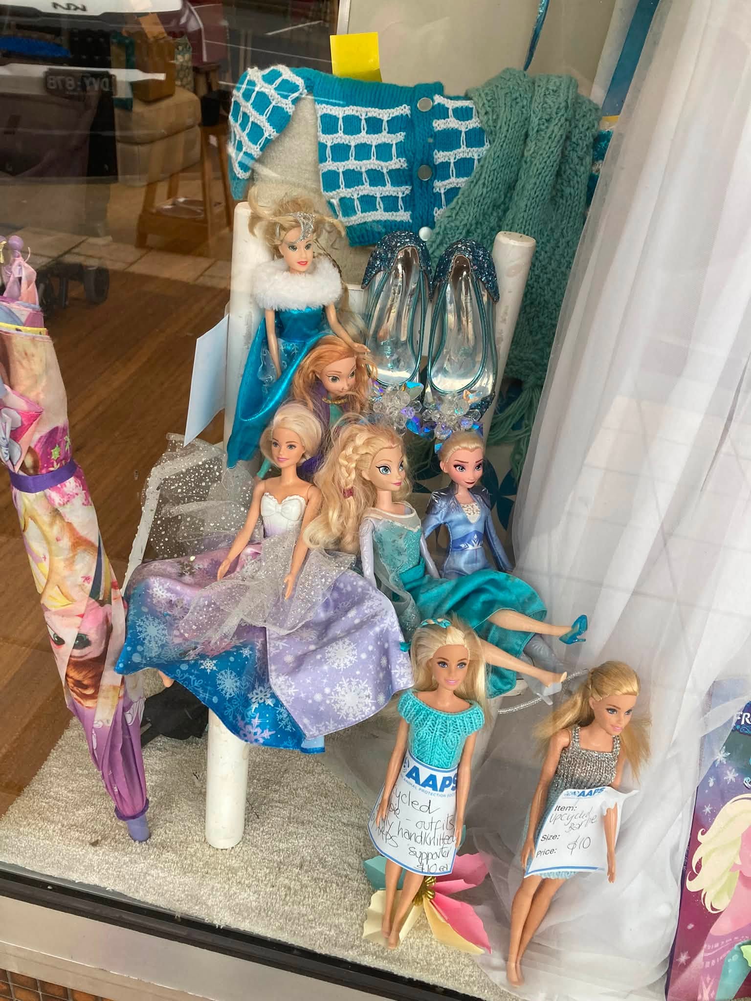 Frozen frenzy at AAPS Op Shop Cheltenham, with children’s Elsa and Anna costumes, dolls, toys, glitter shoes and wintery clothing in store. Visible prices include a Frozen backpack for $5, a polar-bear soft toy for $8, an upcycled doll for $10, and a white crystal dress in size 12–14 for $45.