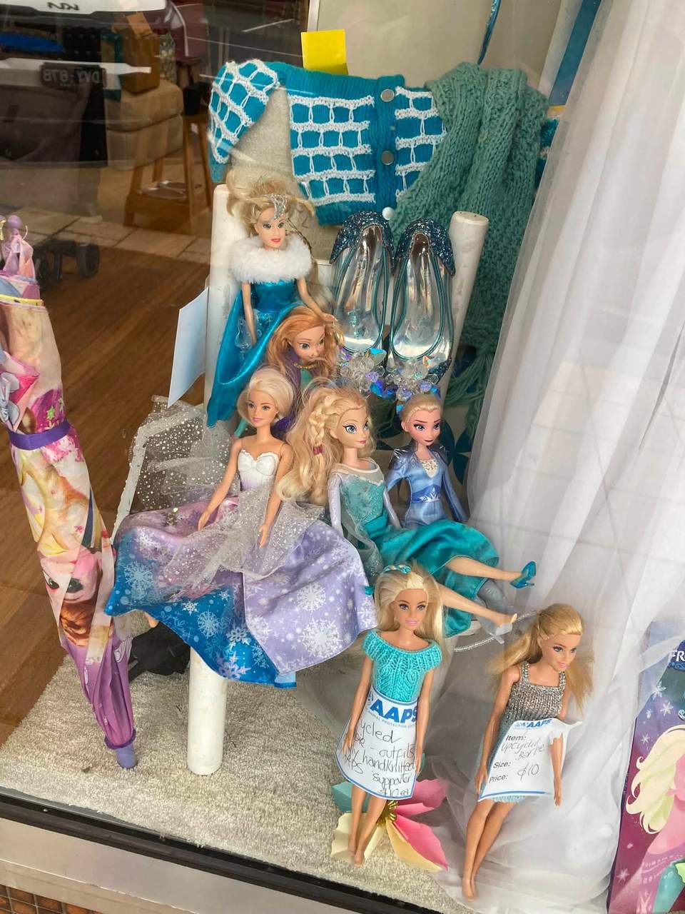 Frozen frenzy at AAPS Op Shop Cheltenham, with children’s Elsa and Anna costumes, dolls, toys, glitter shoes and wintery clothing in store. Visible prices include a Frozen backpack for $5, a polar-bear soft toy for $8, an upcycled doll for $10, and a white crystal dress in size 12–14 for $45.