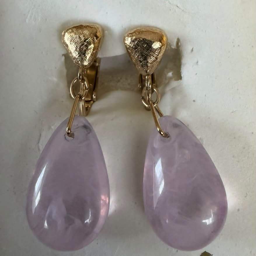 A vintage gold-toned clip-on earring featuring a textured upper component and a tumbled, teardrop-shaped pale purple stone drop that resembles amethyst. $45